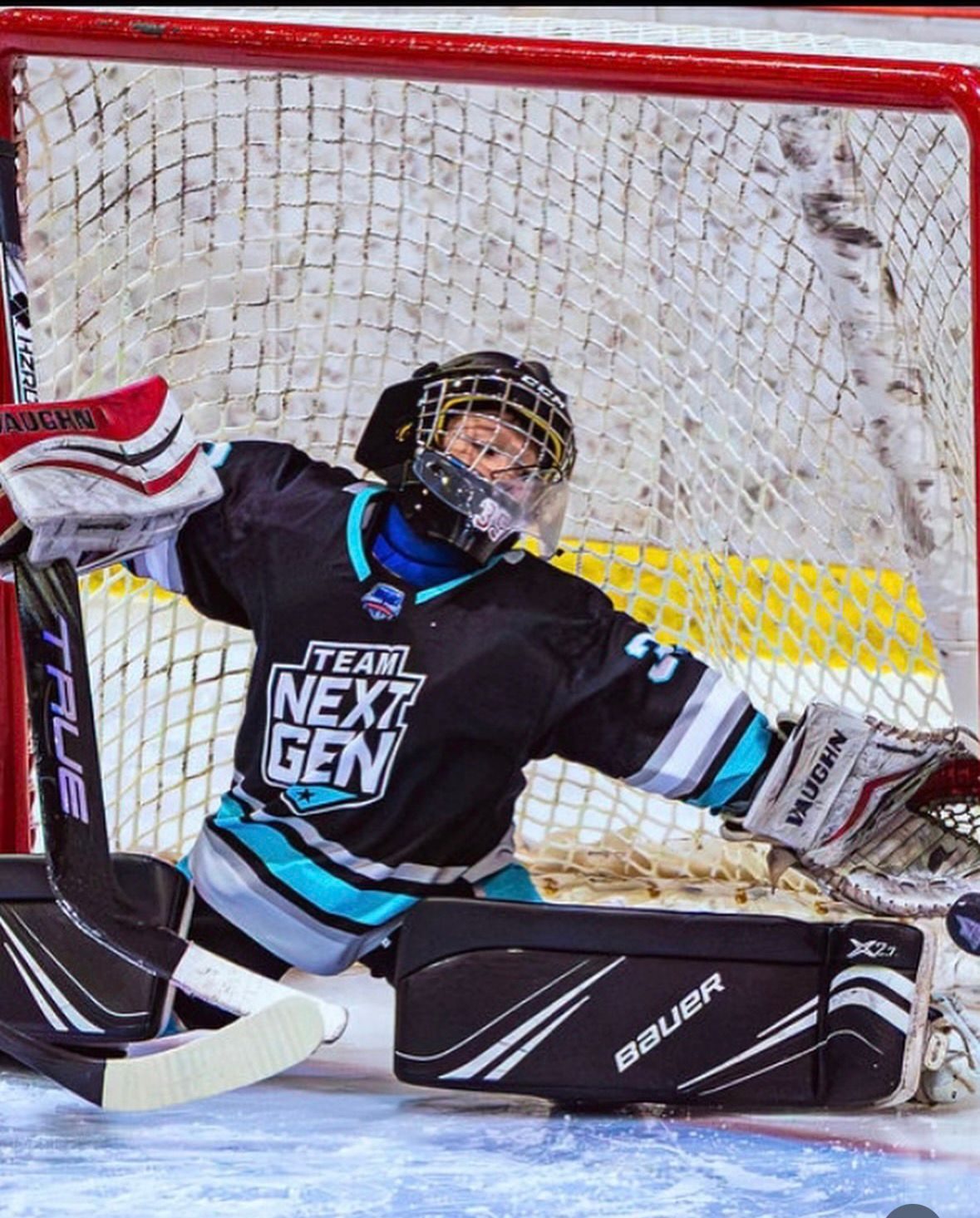 A young Team NexGen goaltender in full pads crouches in the crease tracking the puck during a game