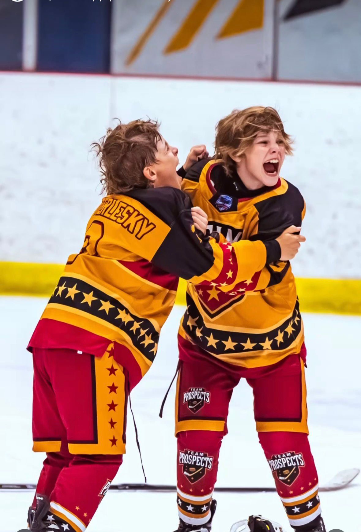 Two teammates in gold and red Team Prospects jerseys shout and hug each other in celebration after a goal